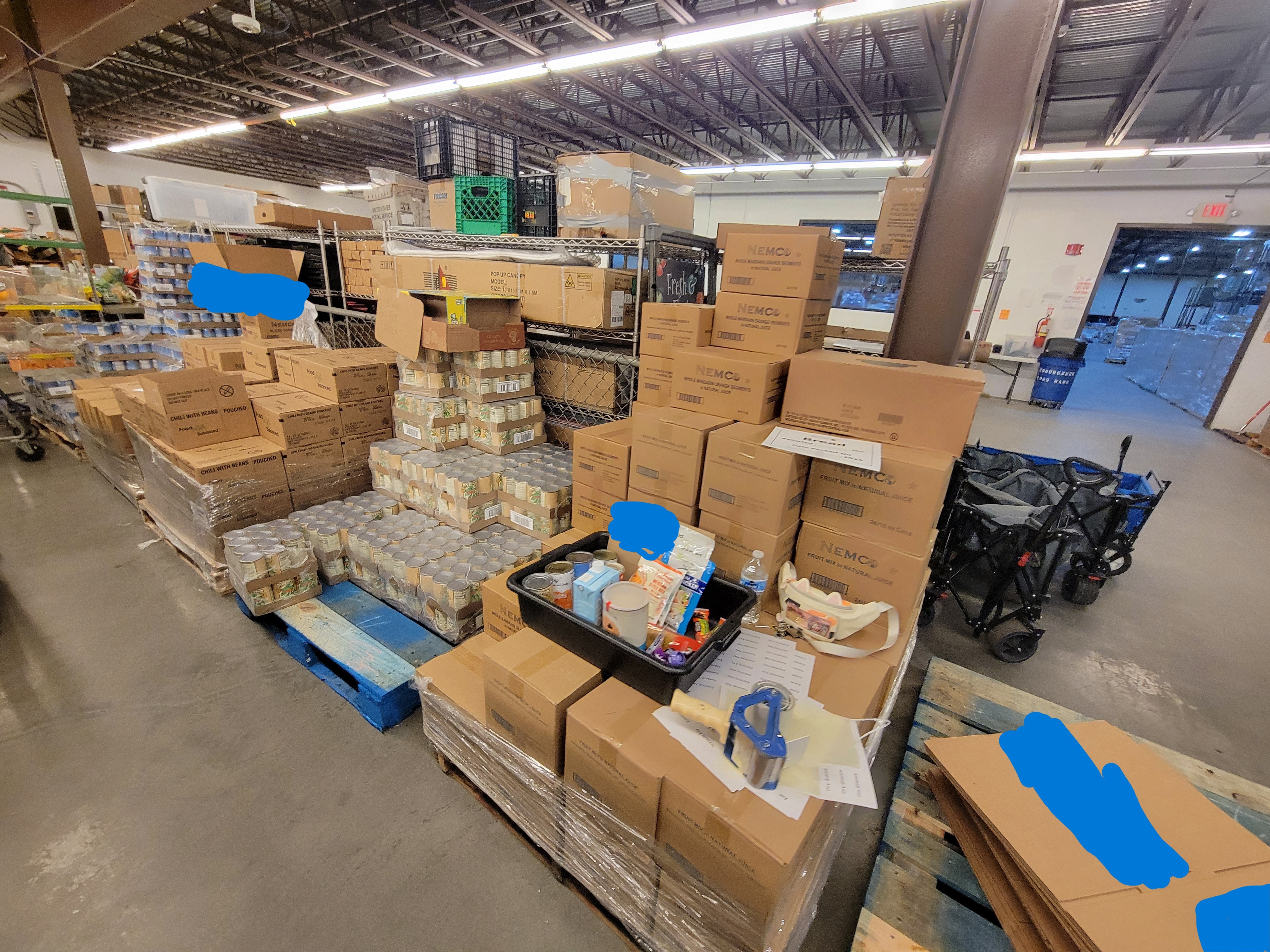 Pallets of food with a sample delivery box, cat fanny, labels, water bottle, and tape gun on top of one.